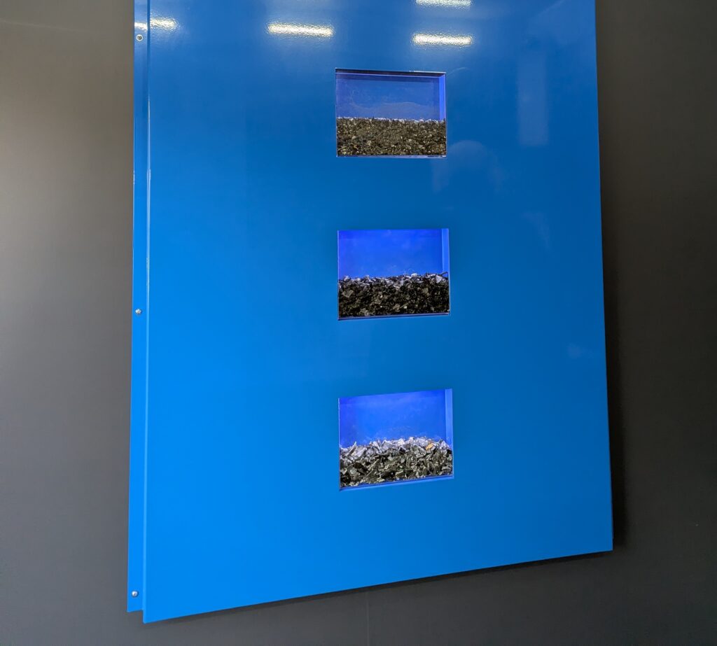 Blue display showing stages of shredded and recycled hard-drive material produced through BCCIT's secure disposal service.