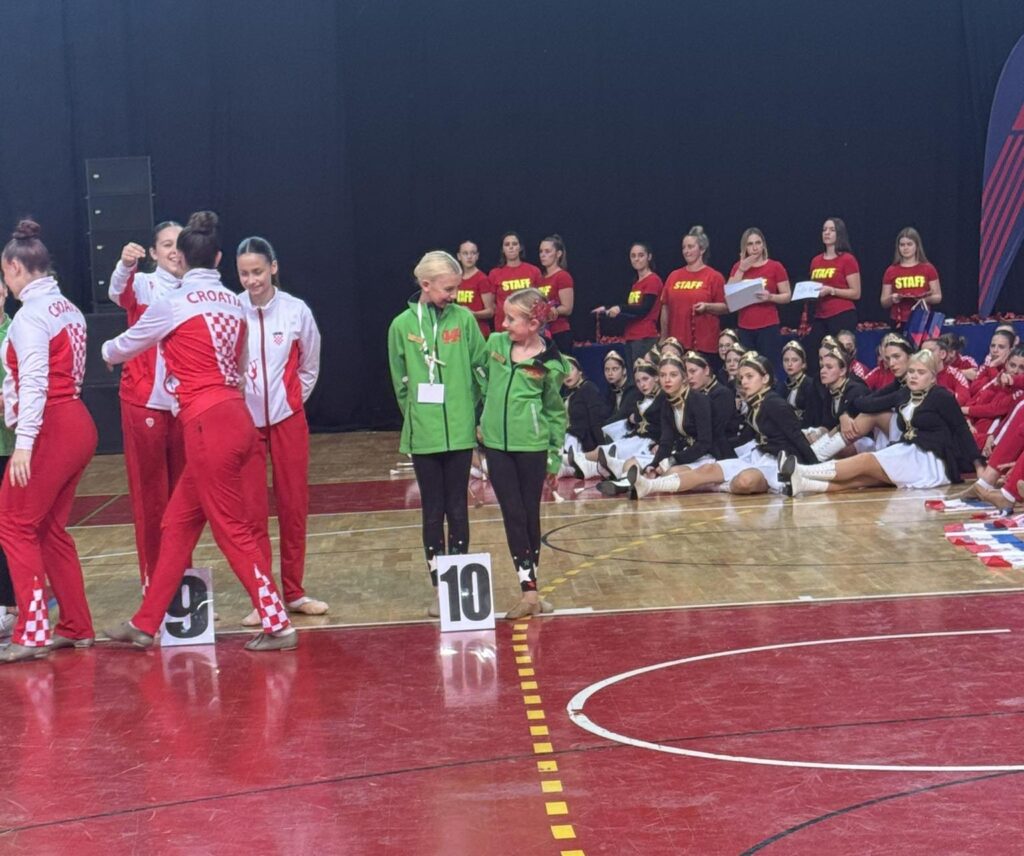 Chloe Brettle and Maisie James standing on the competition floor in green Wales tracksuits after placing tenth in their duet category.