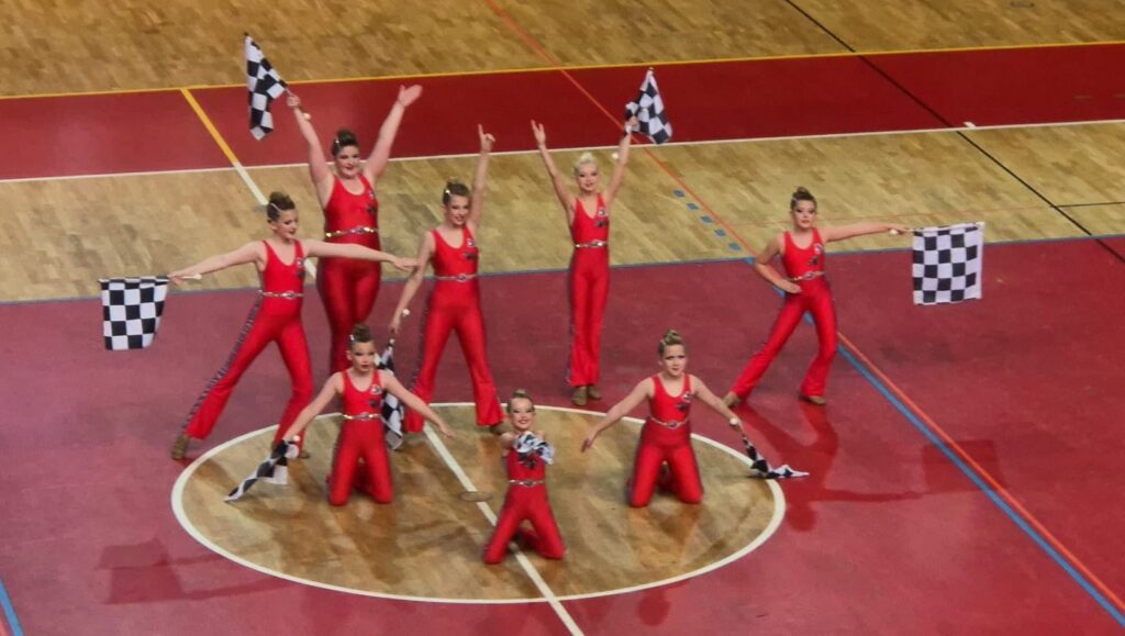 Welsh majorette team performing a group routine in red outfits with checkered flags raised in formation.