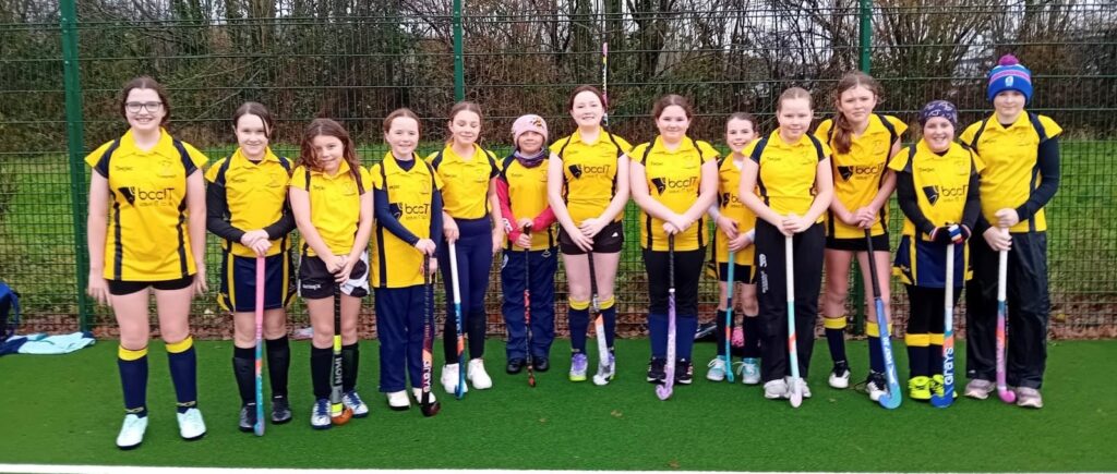 Clwb Hoci Llandysul junior girls' hockey team in yellow kits displaying the bccit logo in front of the goal on the Ysgol Bro Teifi astro pitch