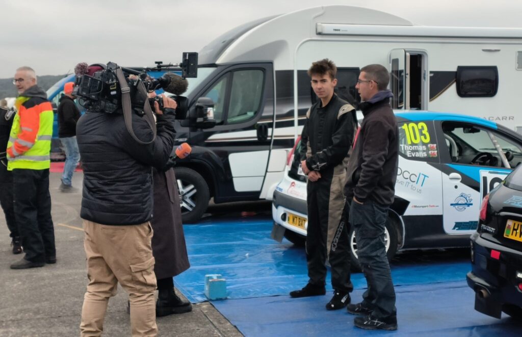 Ioan Thomas being interviewed during rally event with Peugeot 107 and BCC IT sponsorship visible