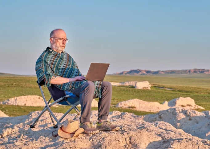Stock image of an IT user in West Wales working from a laptop in a remote mountainous region, symbolising the May bank Holiday in IT