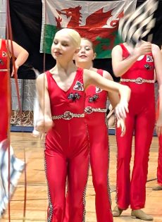 Welsh Majorette team performing in red costumes with a Welsh flag in the background.
