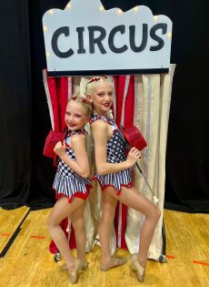 chloe-and-maisie posing together during their duet routine in front of a circus tent.